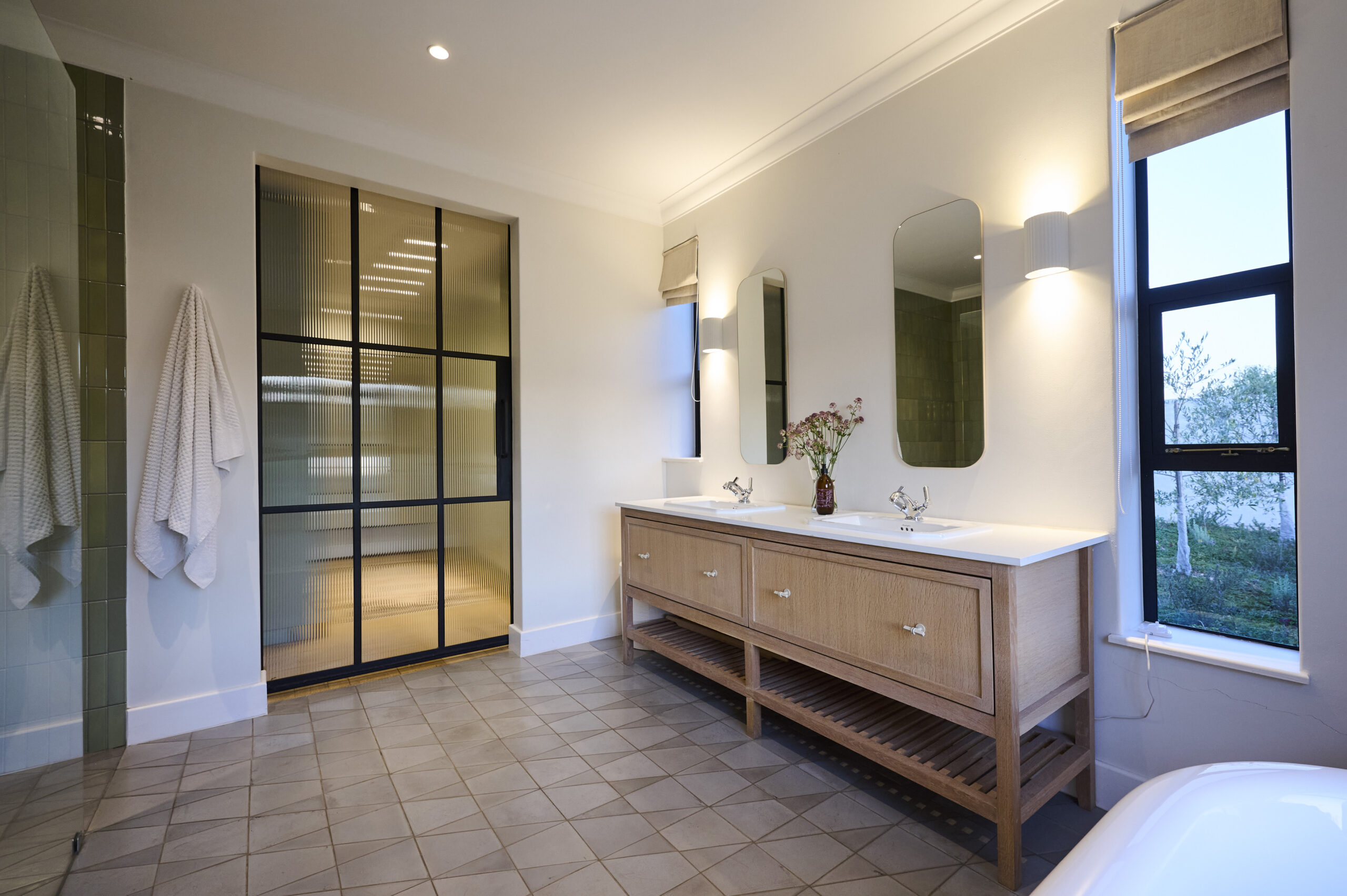 Bright bathroom with a freestanding white bathtub positioned under a black-framed window.