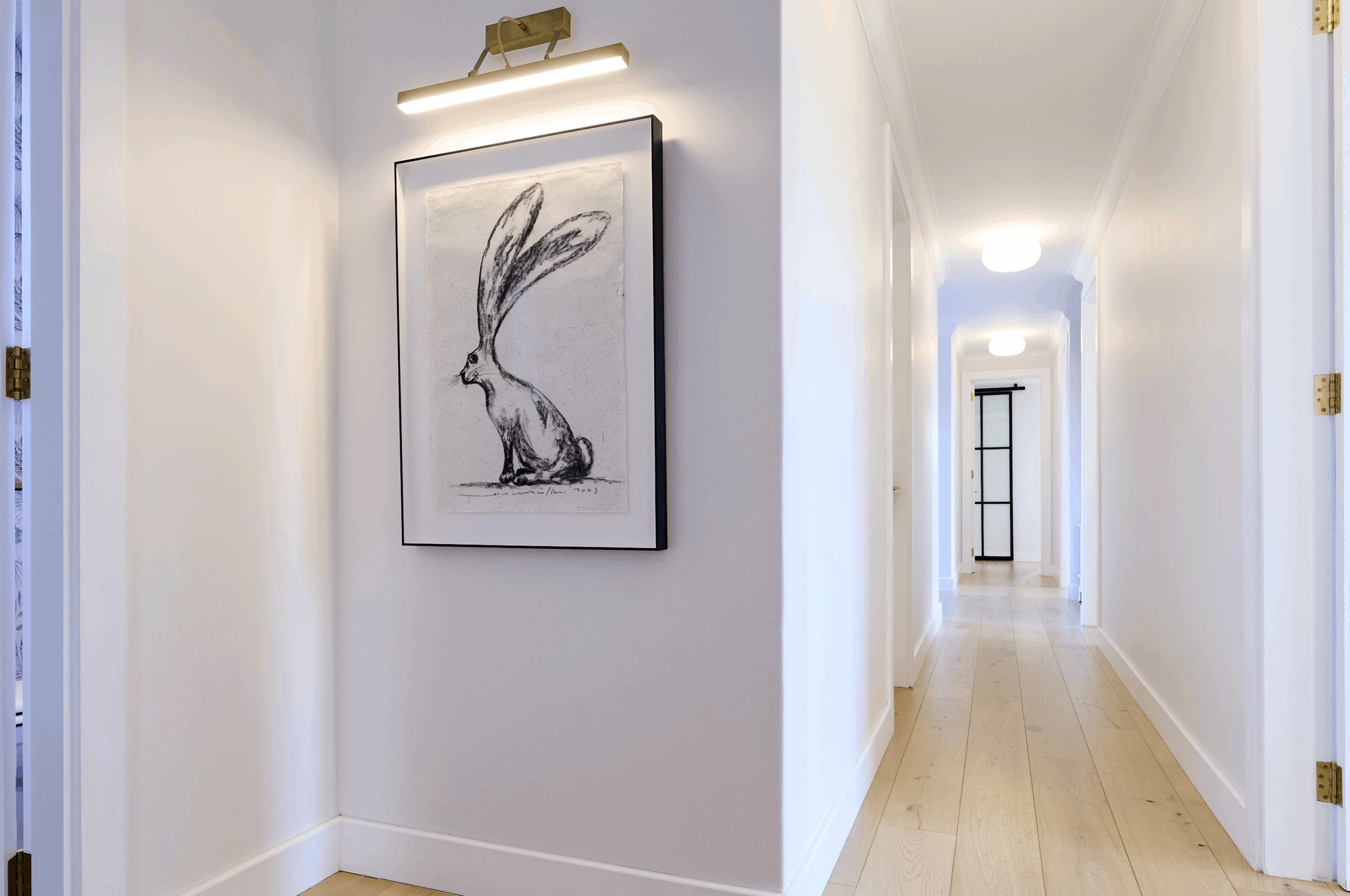 Clean white interior hallway with light hardwood floors and framed artwork.