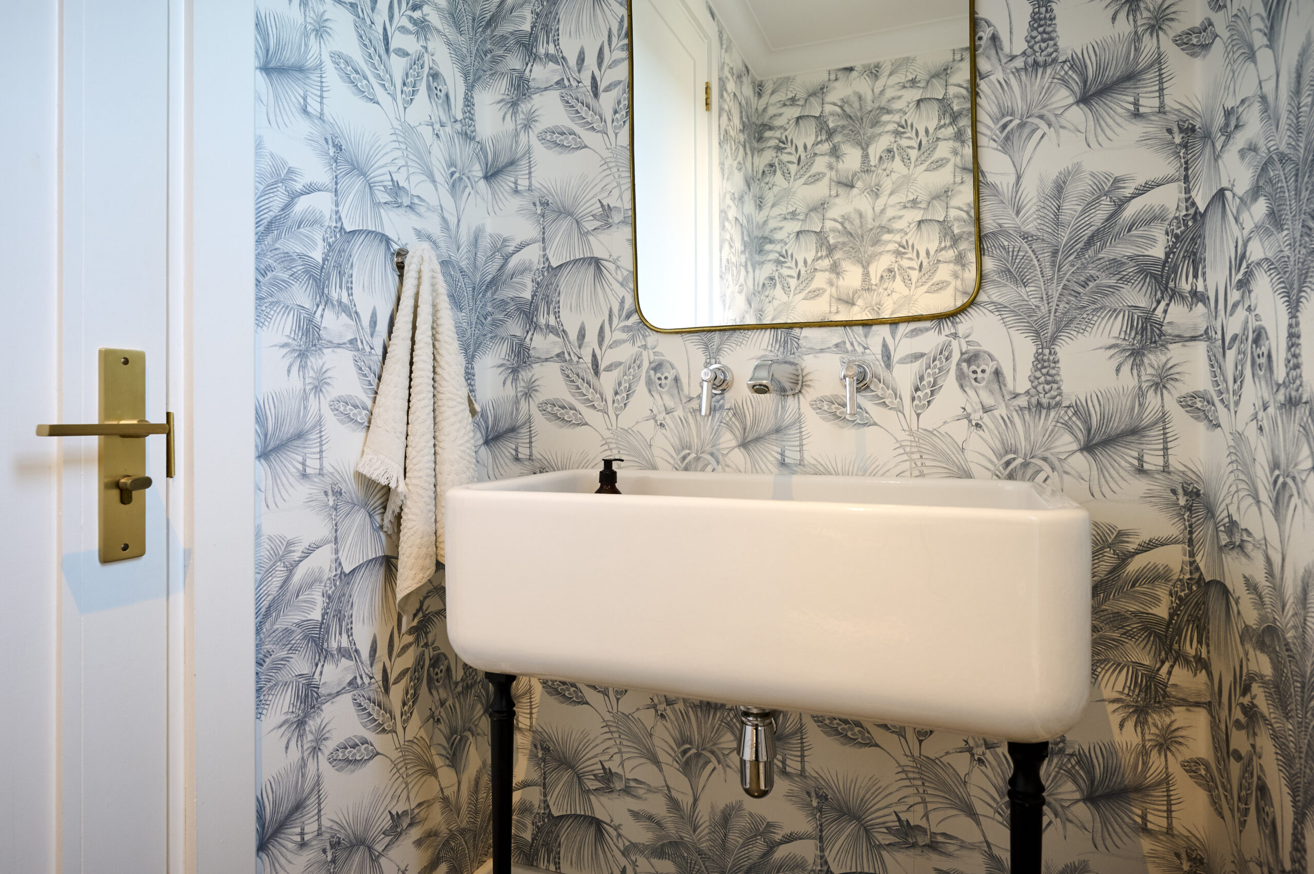 Compact powder room featuring patterned blue wallpaper and a vintage-style wall-mounted trough sink.