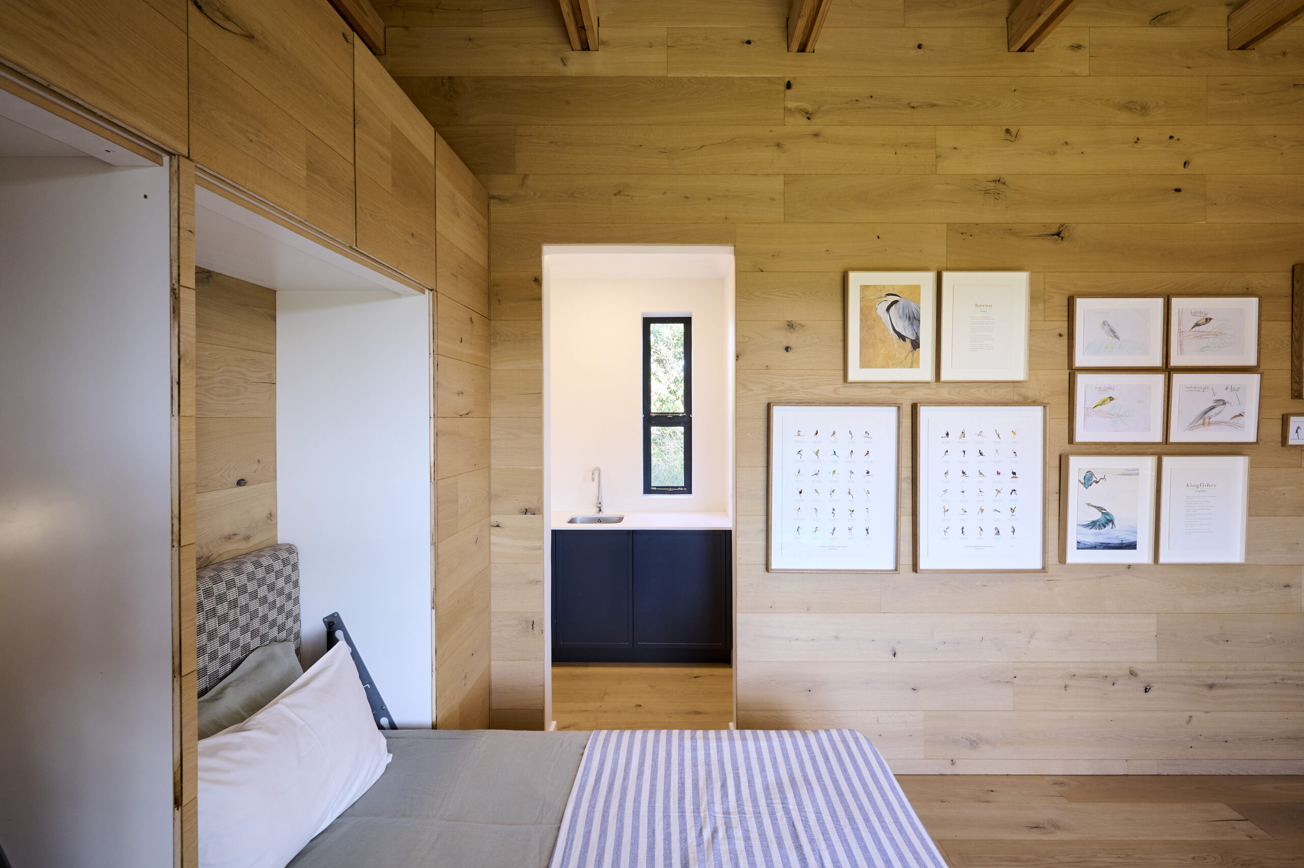 Compact timber-clad bedroom showing a built-in bed and black accents.