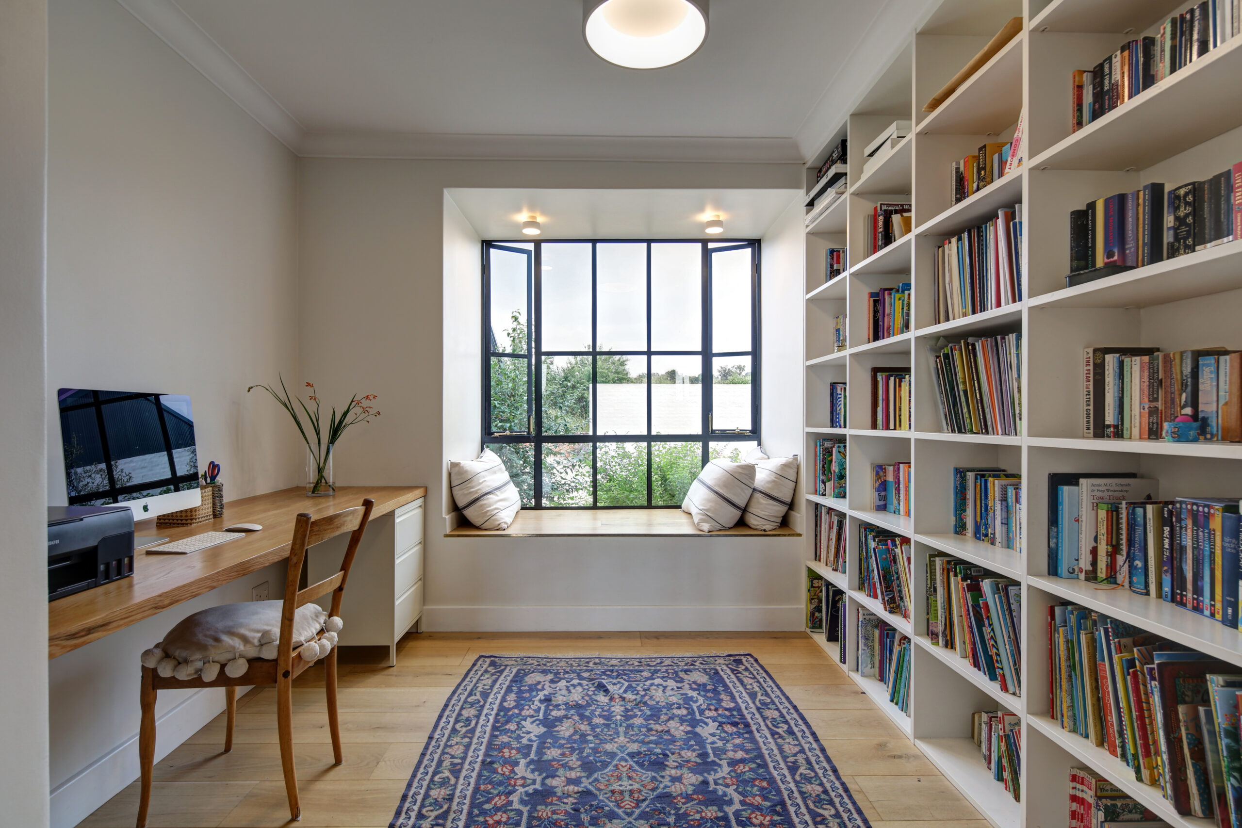 Cozy reading nook with a built-in window seat, throw pillows, and adjacent bookshelves.