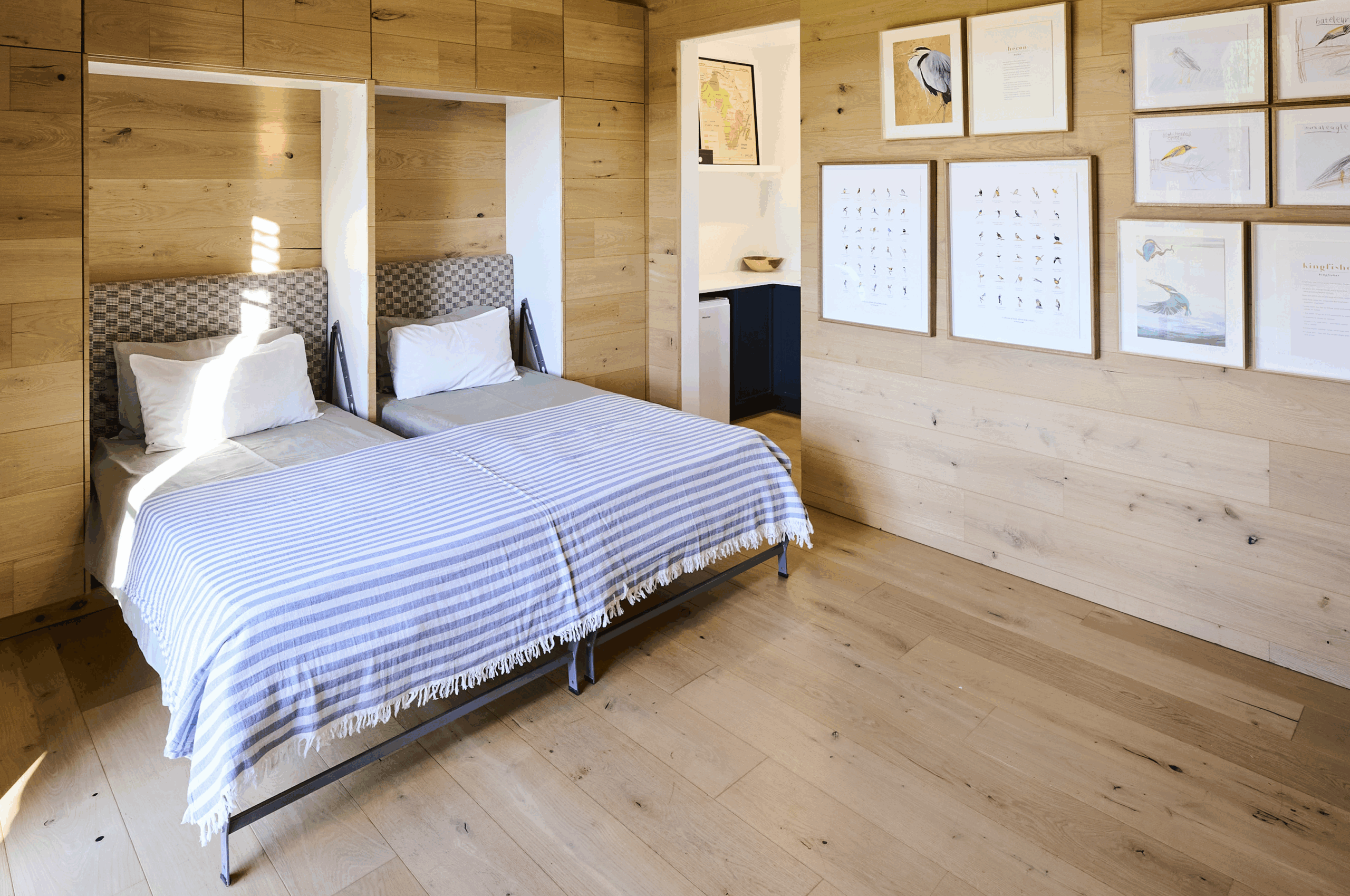 Minimalist bedroom entirely lined in natural timber paneling with framed sketches on the wall.