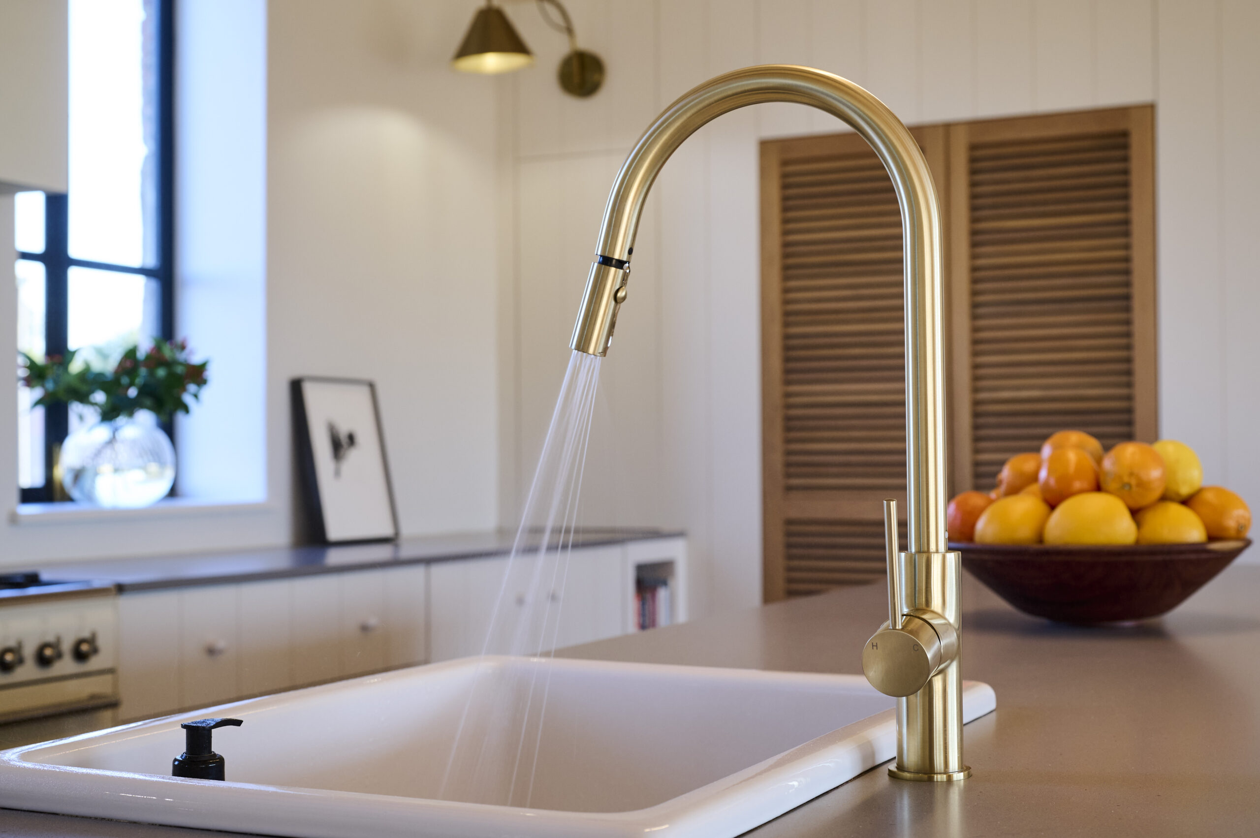 Close-up of a modern white kitchen sink with a sleek brushed gold gooseneck faucet.