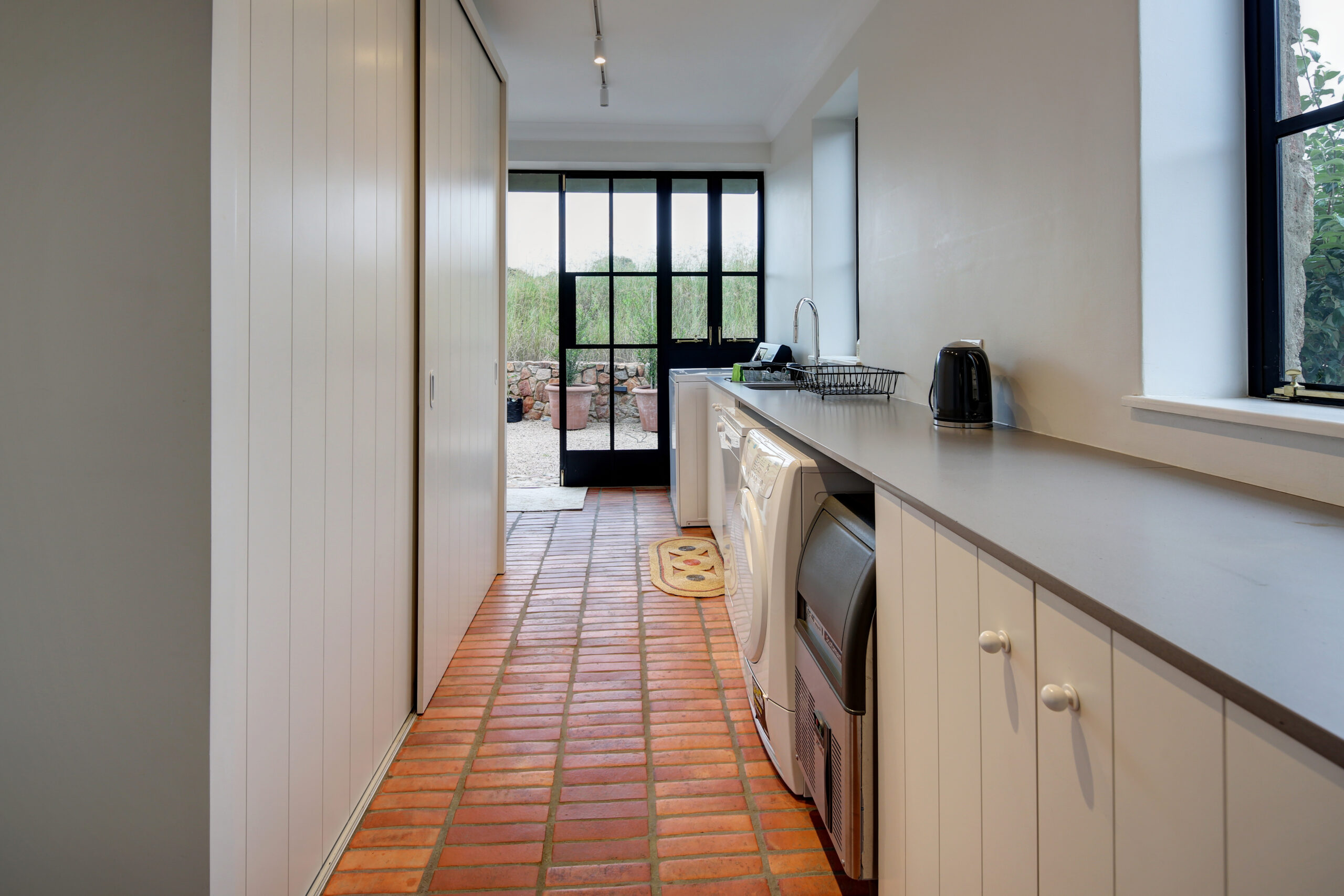 Clean scullery or laundry room with terracotta floor tiles and long storage countertops.