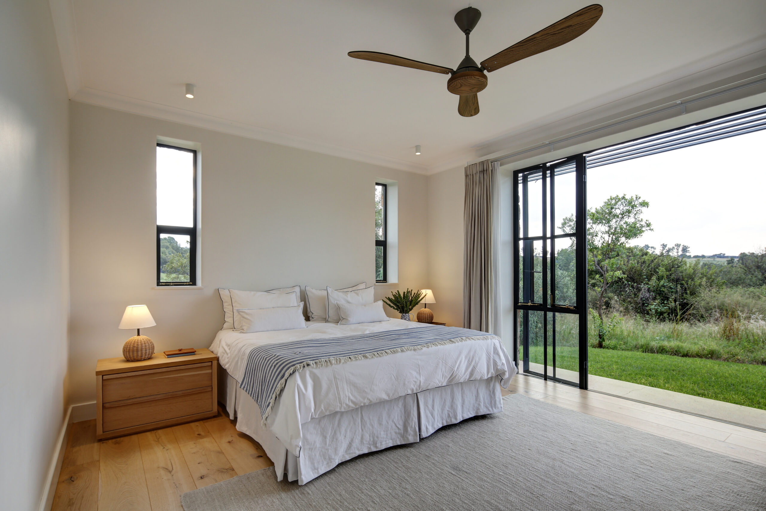 Spacious master bedroom with a ceiling fan, light wood floors, and large sliding doors opening to the patio.