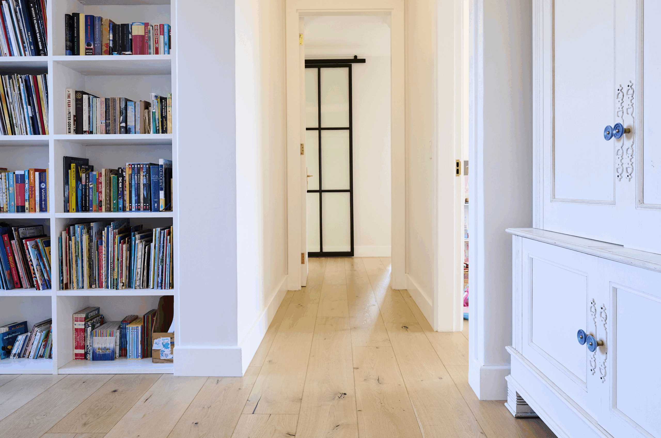 White hallway with built-in floor-to-ceiling bookshelves filled with books.