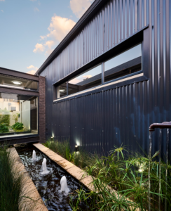 Close-up of the linear pond and fountains at dusk, with warm lighting reflecting off the black corrugated iron.