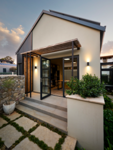 Side view of the master suite wing featuring a light steel and Thermory pine pergola over a glass door.
