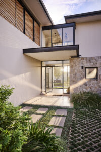 Close up of a low-angle shot of a modern home entrance showing glass doors and a geometric grass-and-paver driveway.