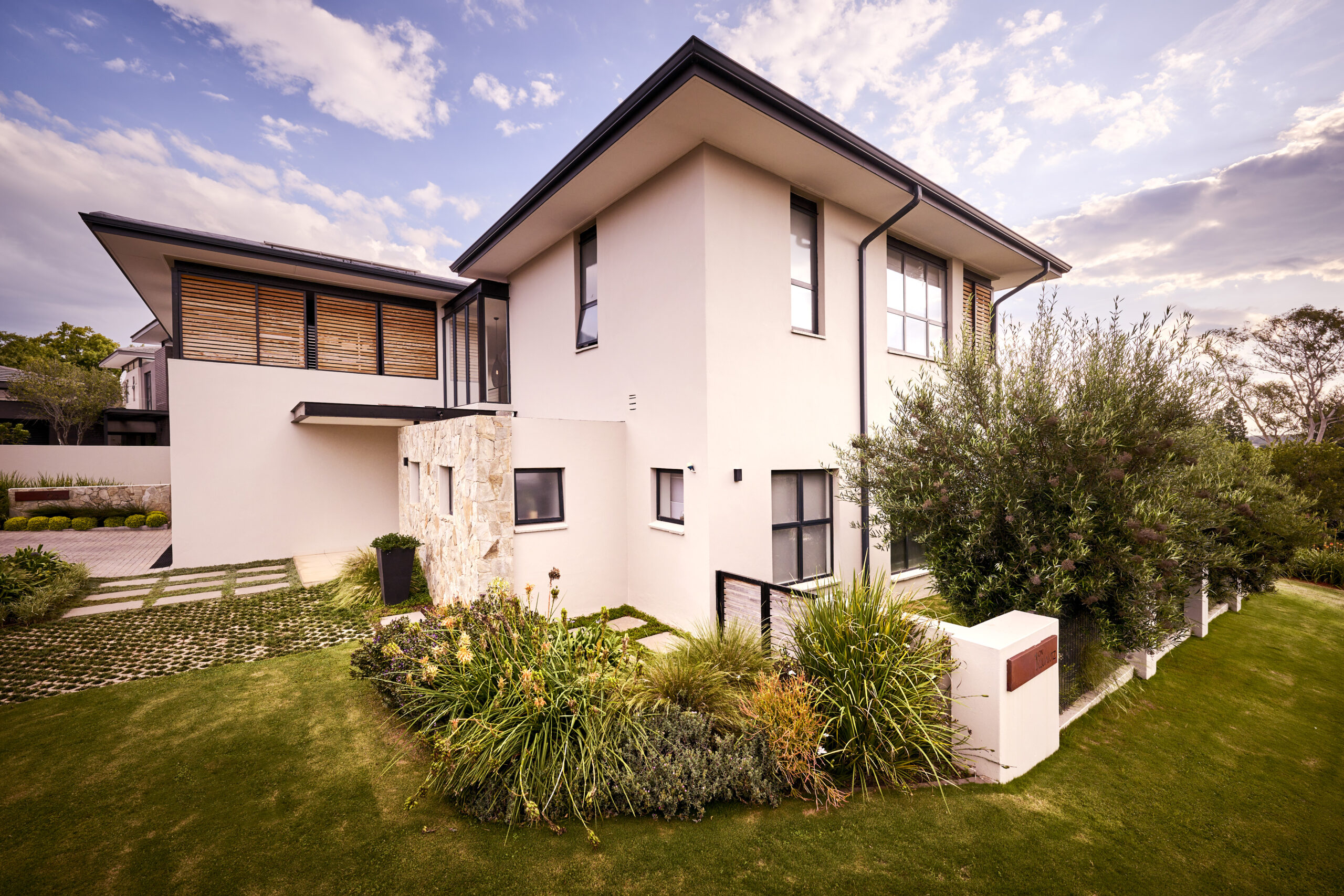 contemporary-architecture-garden-view Side profile of a modern white house with a flat roof, large windows, and manicured green landscaping.