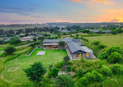 Aerial drone photograph highlighting the L-shaped architecture of the contemporary home nestled within a green, rural landscape.
