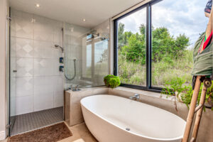 White oval freestanding bathtub positioned next to a large window overlooking a lush green garden.