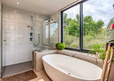 White oval freestanding bathtub positioned next to a large window overlooking a lush green garden.