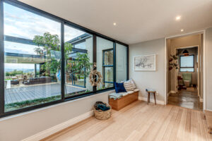 Bright hallway with large windows, light wood flooring, and a built-in wooden storage bench with accent cushions.