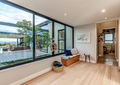 Bright hallway with large windows, light wood flooring, and a built-in wooden storage bench with accent cushions.