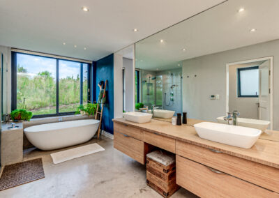 Contemporary bathroom featuring a long floating wooden double vanity, white vessel sinks, a large mirror, and a freestanding white bathtub.