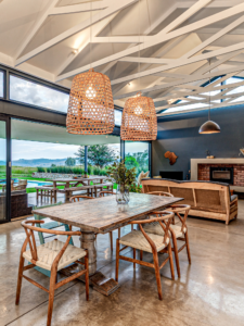 Contemporary open-plan dining room featuring a rustic wooden table, wishbone chairs, woven rattan basket pendant lights, and large sliding glass doors opening to a patio.