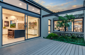 Grey wooden deck outside open kitchen sliding doors, showcasing a feature stone retaining wall and indoor-outdoor living design.
