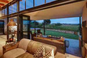 Interior living area with a brown leather sofa and large glass walls showing a panoramic view of the landscape.