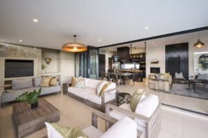 Bright living room featuring a long white sofa, colorful accent pillows, and large glass windows overlooking the garden.