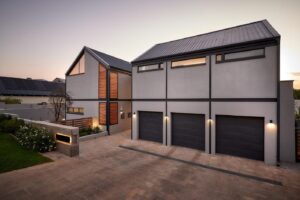 Street-side view of a modern industrial barn-style home in Waterfall Estate featuring grey walls and black steel portal frames