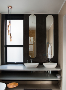 Stylish bathroom featuring two vessel sinks on a floating vanity with three tall, oval-shaped mirrors and hanging pendant bulbs.