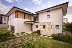 Front view of a contemporary two-story white house featuring a natural stone accent wall and wooden window louvers.