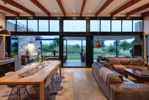 Modern kitchen featuring a large wooden dining table, pendant lighting, and floor-to-ceiling glass doors.
