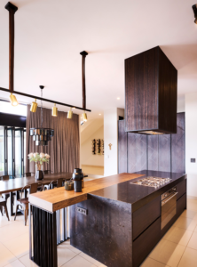 Sleek industrial kitchen featuring a black minimalist island with a wooden breakfast bar extension and integrated gas stovetop.