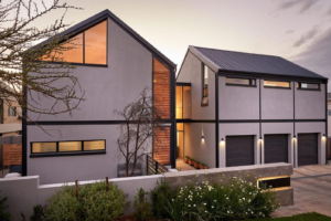 A lit glass entrance lobby at dusk connecting the two main wings of the contemporary family home.
