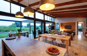 Modern open plan kitchen with view to spacious living room with leather sofas, wood-beamed ceilings, and a view to the outdoor patio.