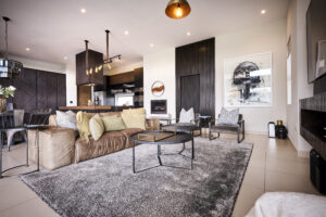 Spacious open-plan living area with a grey rug, contemporary furniture, and view towards the kitchen and dining area.