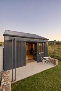 Modern dark corrugated metal studio cottage featuring a small concrete patio.