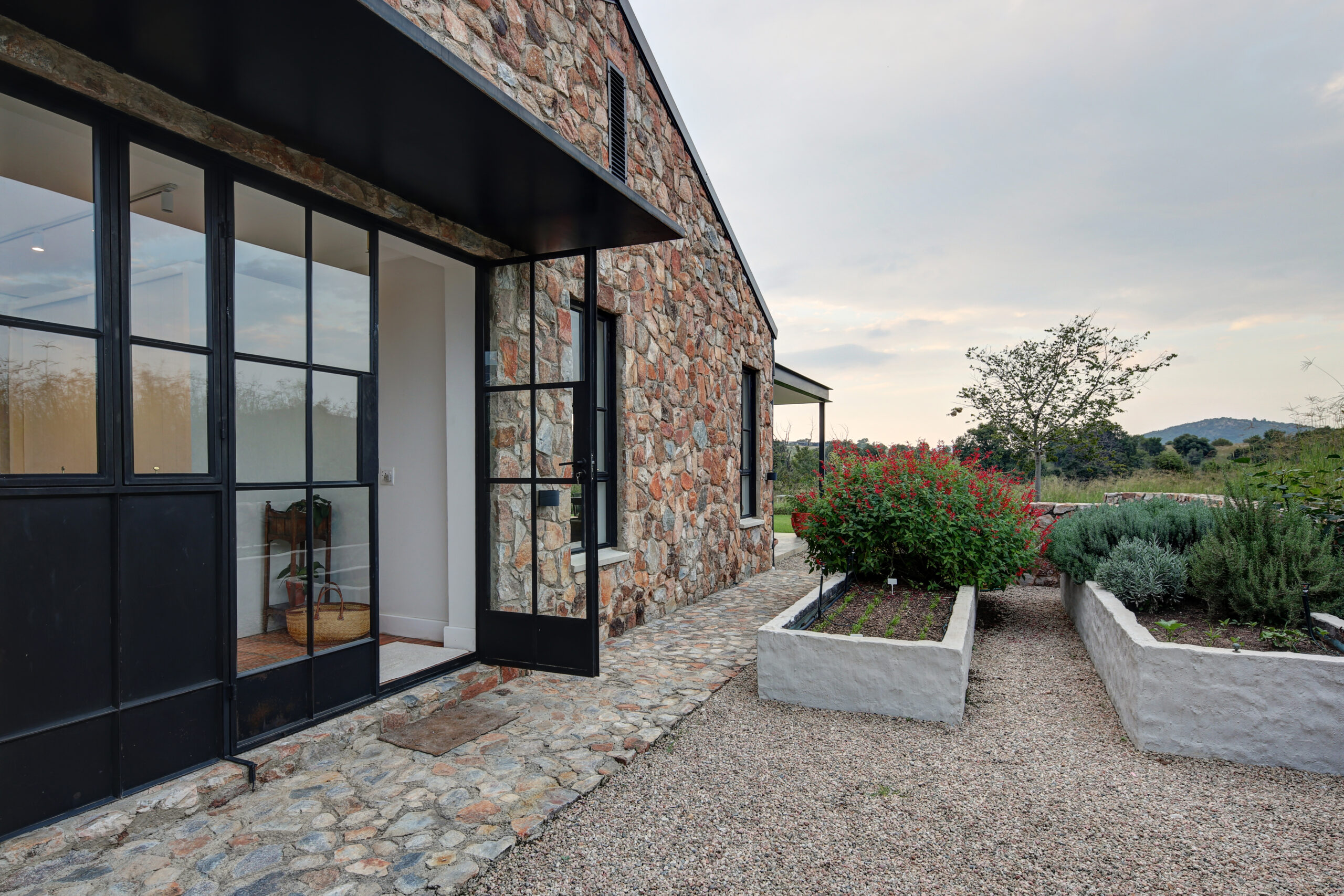 Narrow gravel side path next to the stone wall exterior with raised concrete planter boxes