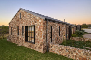 Perspective view of the stone house's gable wall showing clean rooflines, black-framed windows, and manicured lawn.
