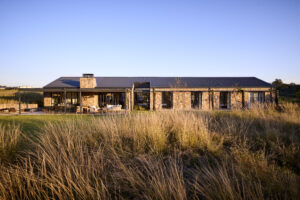 Wide panoramic view of the low-profile stone house integrated into the natural grassy countryside landscape.