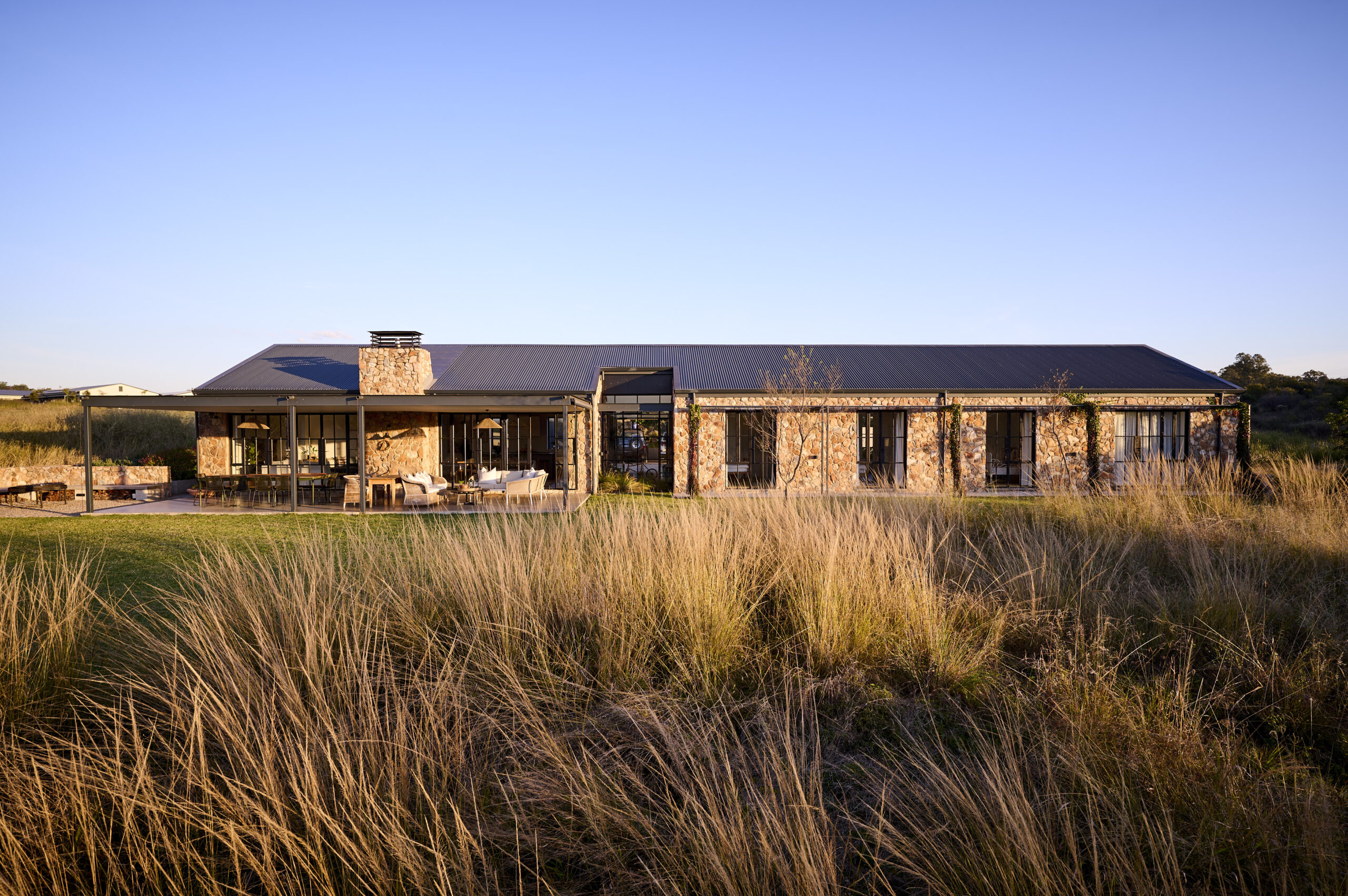 Wide panoramic view of the low-profile stone house integrated into the natural grassy countryside landscape.