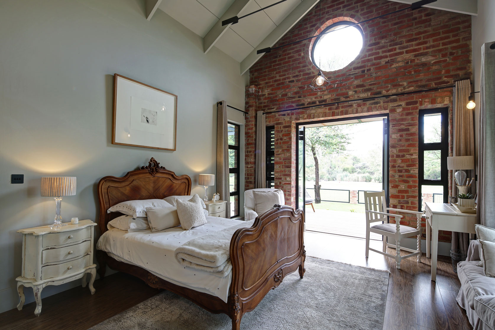 Bedroom with exposed stock brick wall, porthole window and a steel & glass door opening onto private deck