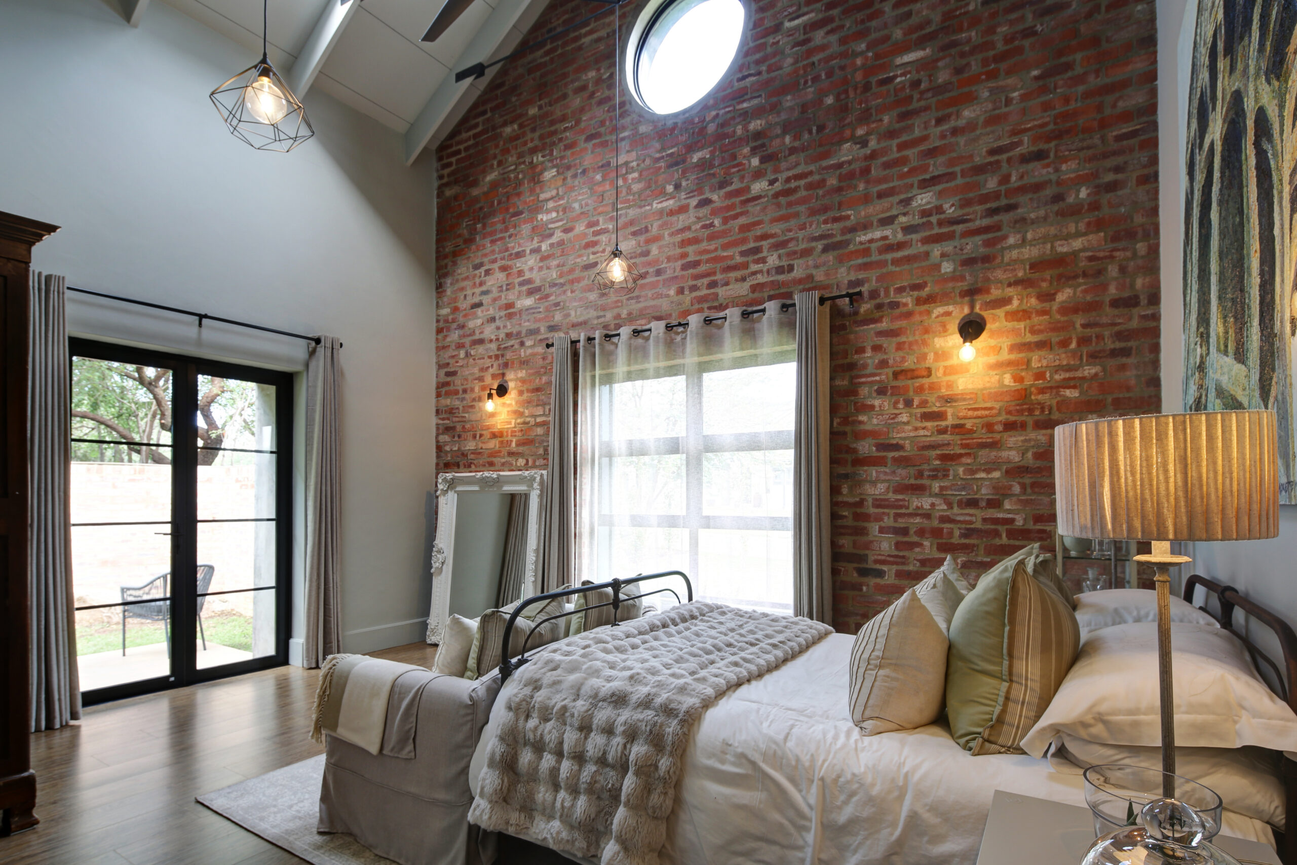 Bedroom with exposed stock brick wall and porthole window with a steel & glass door opening onto private deck