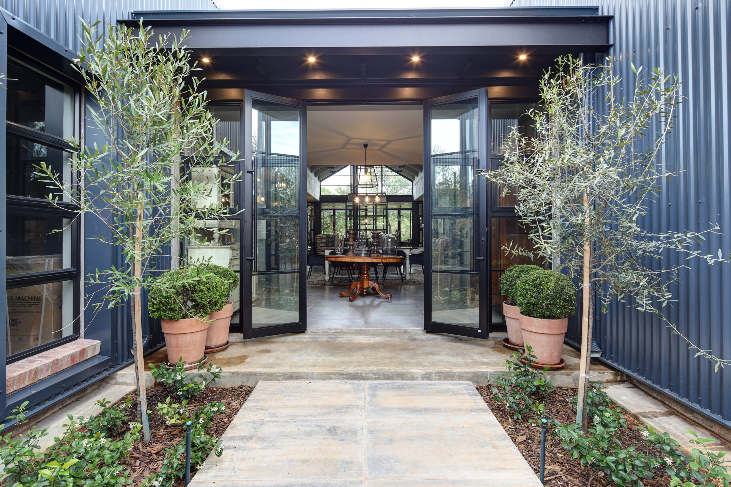 View of dining room from courtyard entrance, with courtyard garden and corrugated sheeting clad sheds