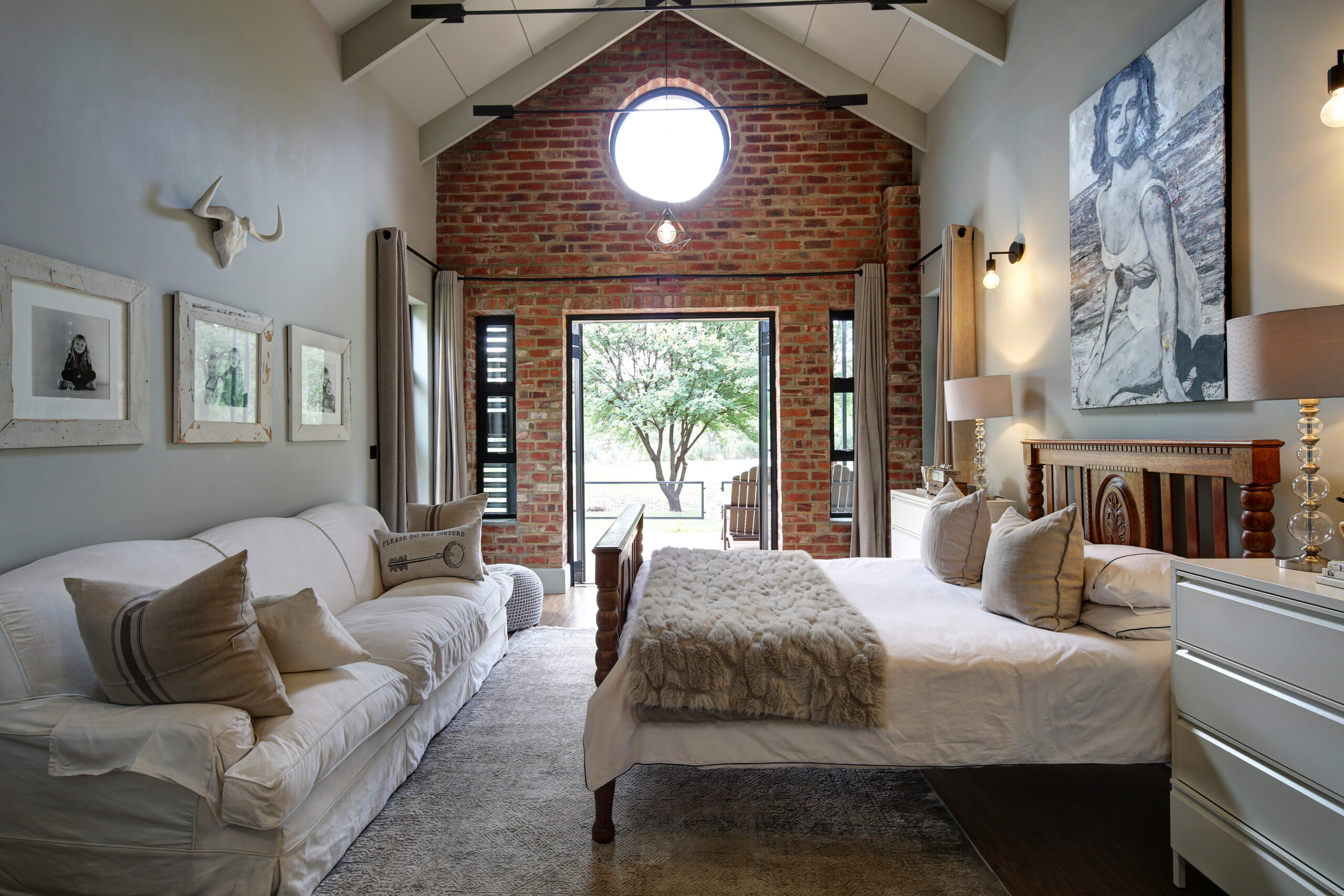 Main bedroom with exposed stock brick wall and porthole window with a steel & glass door opening onto private deck